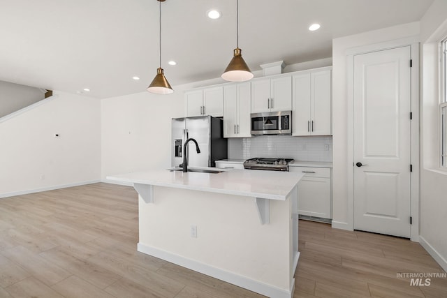 kitchen featuring a kitchen island with sink, stainless steel appliances, white cabinetry, light countertops, and pendant lighting