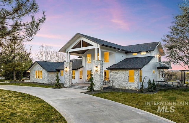 view of front of property featuring covered porch, a lawn, board and batten siding, stone siding, and driveway