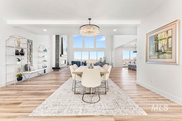 dining room featuring a tile fireplace, a notable chandelier, baseboards, light wood-type flooring, and beamed ceiling