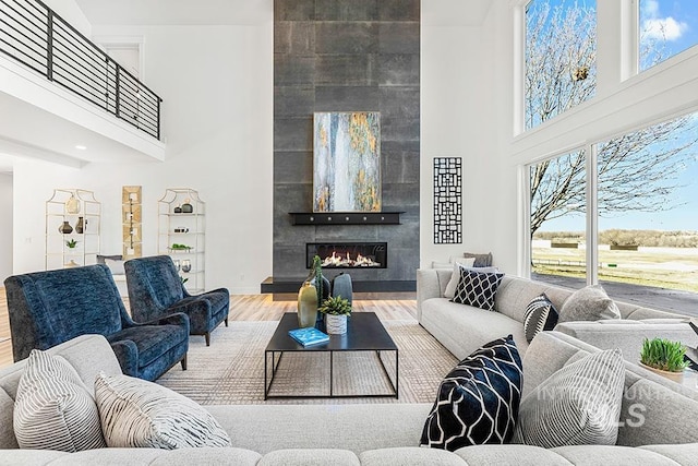 living room with a high ceiling, a tile fireplace, plenty of natural light, and wood finished floors