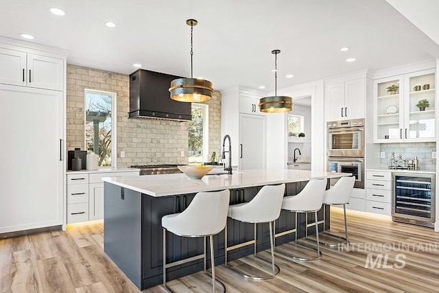 kitchen featuring wine cooler, stainless steel double oven, white cabinetry, light countertops, and custom exhaust hood