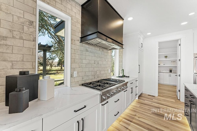 kitchen with stainless steel gas cooktop, white cabinetry, wall chimney range hood, light stone countertops, and light wood-type flooring