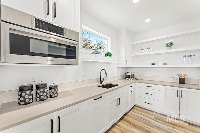 kitchen with white cabinets, oven, light wood-style floors, open shelves, and a sink