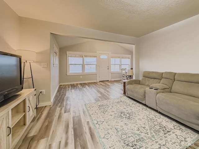 living area featuring baseboards, lofted ceiling, a textured ceiling, and light wood-type flooring