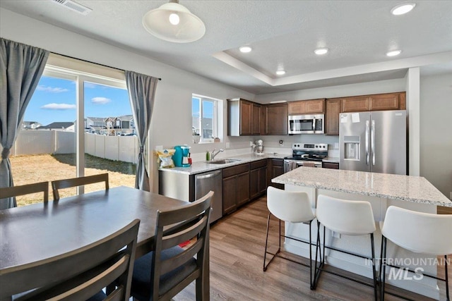 kitchen featuring a tray ceiling, a breakfast bar area, appliances with stainless steel finishes, light wood-style floors, and a sink