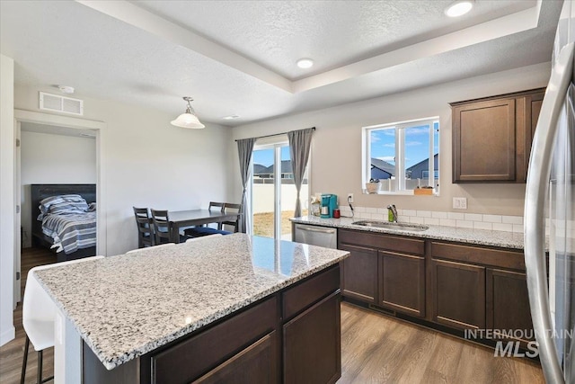 kitchen with a textured ceiling, stainless steel appliances, a sink, a center island, and dark wood-style floors