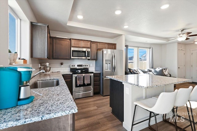 kitchen featuring stainless steel appliances, a sink, a center island, dark wood-style floors, and a kitchen bar