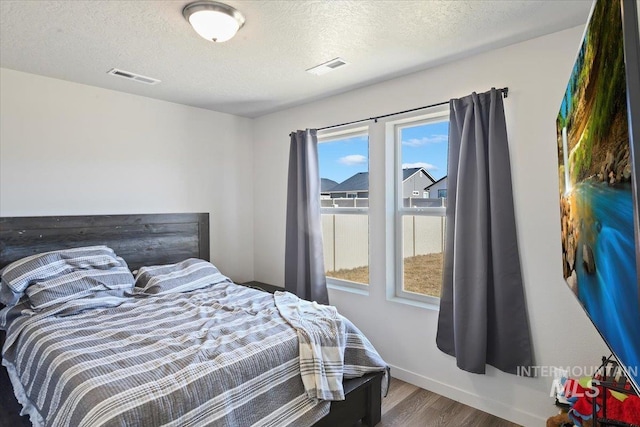 bedroom with a textured ceiling, visible vents, and wood finished floors