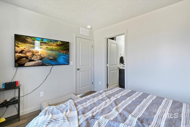 bedroom featuring baseboards, a textured ceiling, visible vents, and wood finished floors