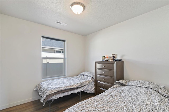 bedroom with visible vents, a textured ceiling, baseboards, and wood finished floors