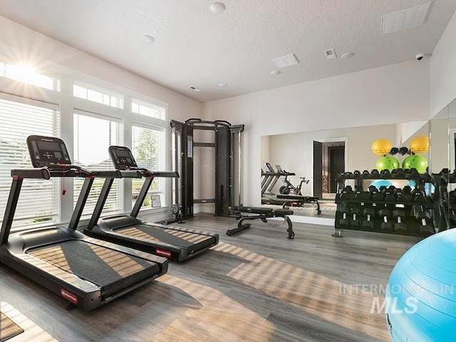 gym featuring visible vents, a textured ceiling, and wood finished floors