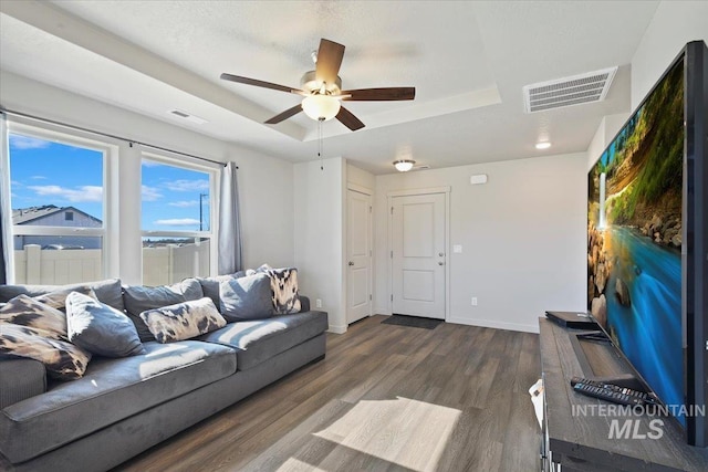 living area featuring dark wood-style floors, baseboards, visible vents, and a tray ceiling