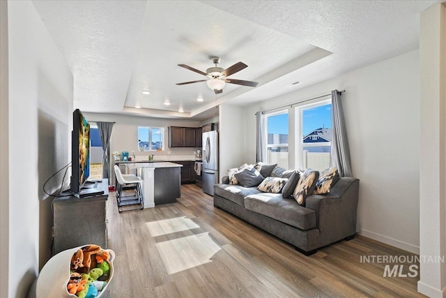 living area with baseboards, light wood-style flooring, a tray ceiling, and a textured ceiling