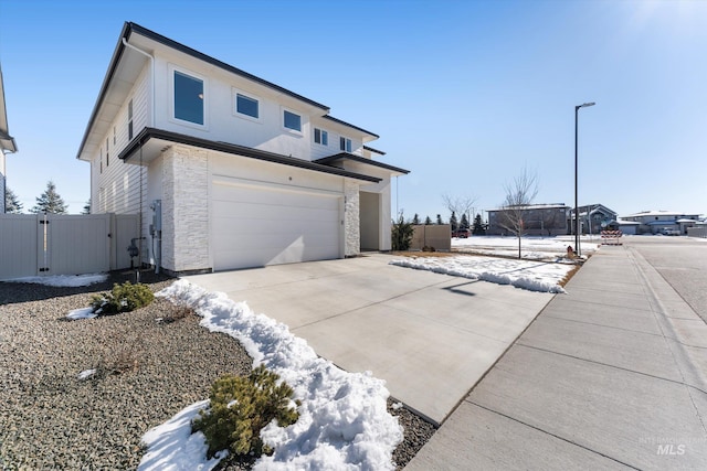 view of home's exterior with an attached garage, a gate, fence, stone siding, and driveway