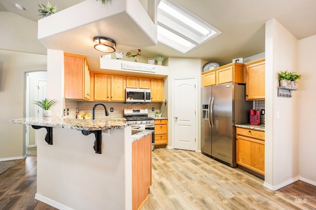 kitchen with stainless steel appliances, lofted ceiling, tasteful backsplash, a peninsula, and a kitchen breakfast bar