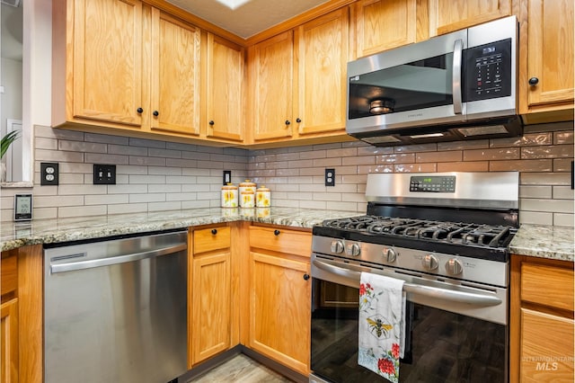 kitchen with stainless steel appliances, light wood-style floors, light stone counters, and decorative backsplash