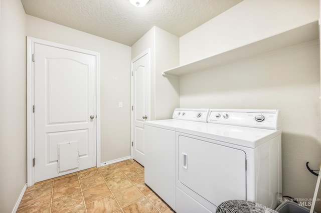 clothes washing area featuring washer and dryer, laundry area, a textured ceiling, and baseboards