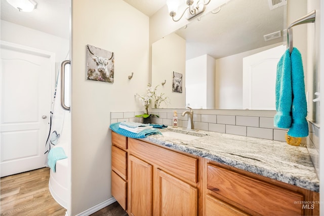 bathroom with visible vents, wood finished floors, vanity, and decorative backsplash