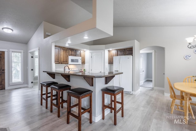 kitchen featuring white appliances, a breakfast bar, lofted ceiling, arched walkways, and light wood-type flooring