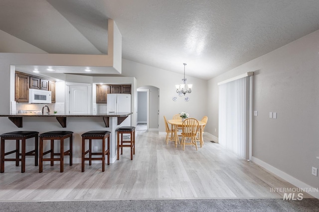 kitchen featuring a breakfast bar, vaulted ceiling, an inviting chandelier, arched walkways, and white appliances