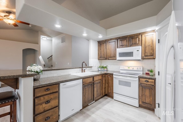 kitchen featuring visible vents, a sink, backsplash, white appliances, and a peninsula