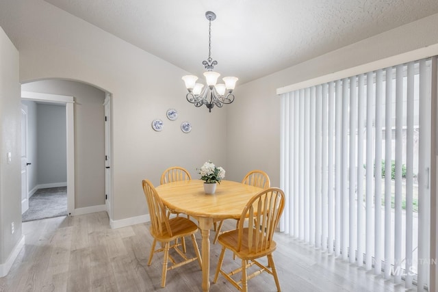 dining room featuring baseboards, arched walkways, a chandelier, and light wood finished floors