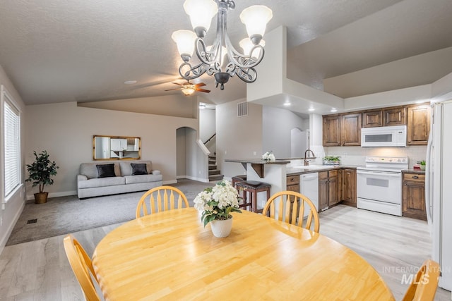 dining space with visible vents, stairway, lofted ceiling, ceiling fan with notable chandelier, and light wood-style floors