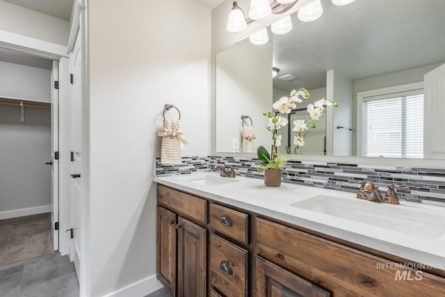 bathroom with a sink, decorative backsplash, baseboards, and double vanity