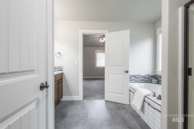 bathroom with baseboards, ceiling fan, vanity, and a garden tub