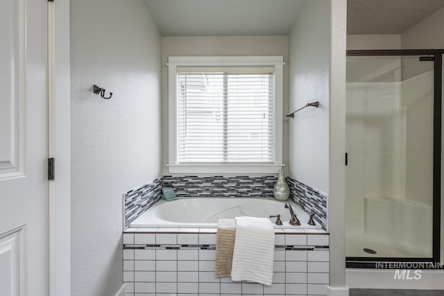 full bathroom with a bath, a stall shower, and a textured wall