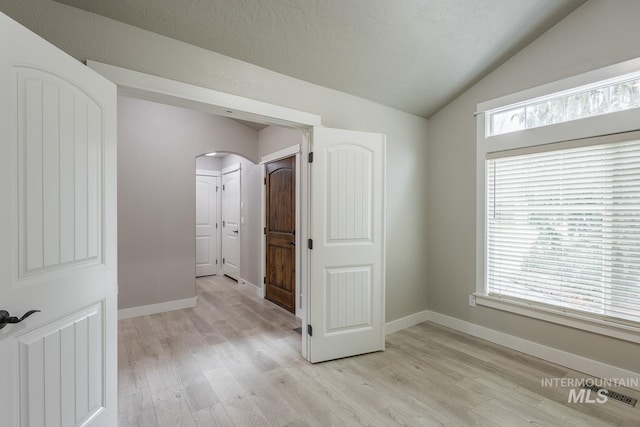 unfurnished bedroom with arched walkways, light wood-type flooring, baseboards, and vaulted ceiling