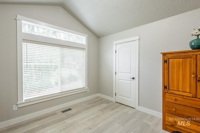 unfurnished bedroom featuring light wood finished floors, visible vents, baseboards, and lofted ceiling