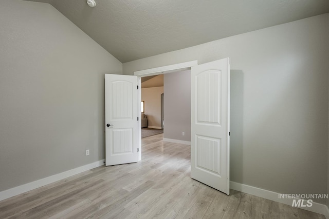 spare room featuring lofted ceiling, light wood-style flooring, baseboards, and a textured ceiling