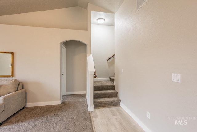 stairs featuring arched walkways, visible vents, baseboards, and vaulted ceiling