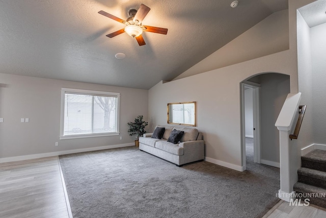 living room featuring baseboards, stairway, lofted ceiling, arched walkways, and a ceiling fan