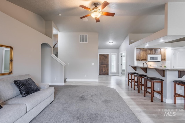 living room with visible vents, ceiling fan, stairway, vaulted ceiling, and light wood-style flooring