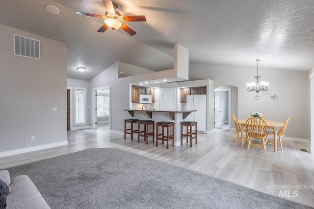 dining area featuring visible vents, lofted ceiling, arched walkways, a textured ceiling, and ceiling fan with notable chandelier