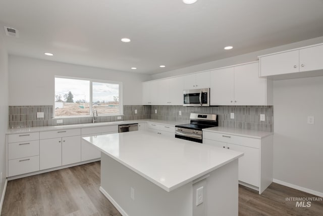 kitchen with a center island, backsplash, light hardwood / wood-style flooring, white cabinetry, and stainless steel appliances