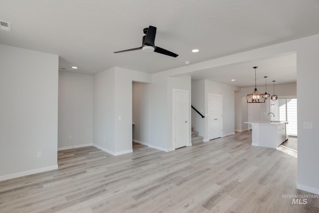 unfurnished living room featuring ceiling fan with notable chandelier, light hardwood / wood-style flooring, and sink