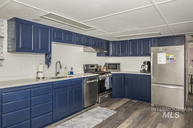kitchen with blue cabinetry, under cabinet range hood, dark wood finished floors, stainless steel appliances, and a sink