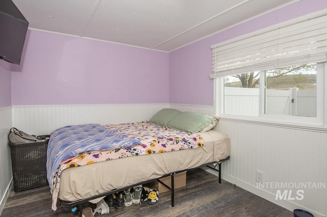 bedroom with ornamental molding, a wainscoted wall, and wood finished floors