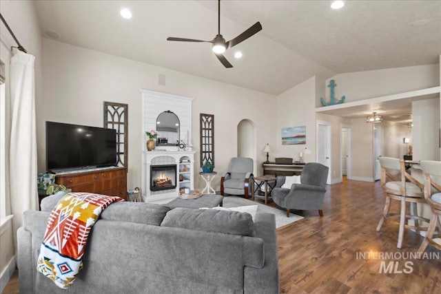 living room with a ceiling fan, recessed lighting, dark wood-style flooring, a warm lit fireplace, and vaulted ceiling