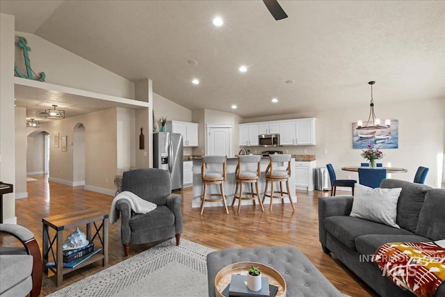 living room with recessed lighting, arched walkways, light wood-style floors, an inviting chandelier, and lofted ceiling