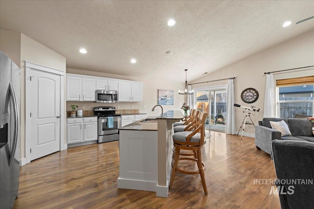 kitchen with lofted ceiling, a sink, white cabinets, appliances with stainless steel finishes, and dark countertops