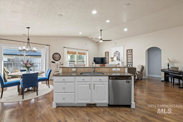 kitchen featuring dark wood-type flooring, vaulted ceiling, stainless steel dishwasher, arched walkways, and a sink