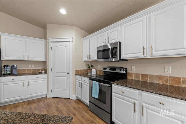 kitchen featuring dark stone countertops, appliances with stainless steel finishes, wood finished floors, and white cabinetry