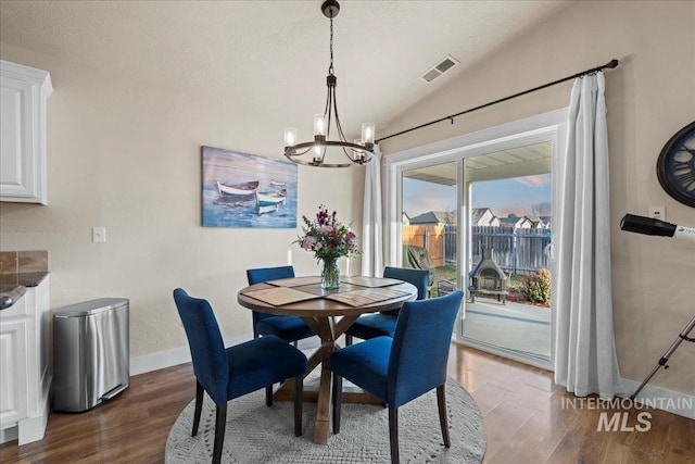 dining area with dark wood finished floors, visible vents, a chandelier, and lofted ceiling