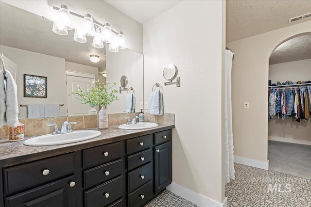 bathroom with double vanity, visible vents, a textured ceiling, and a sink