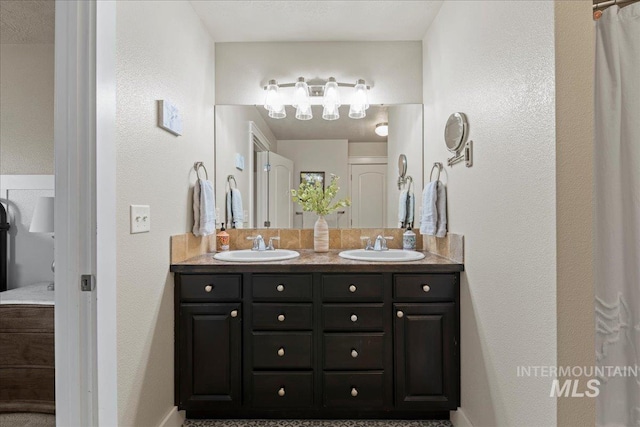 bathroom featuring double vanity, a textured wall, and a sink