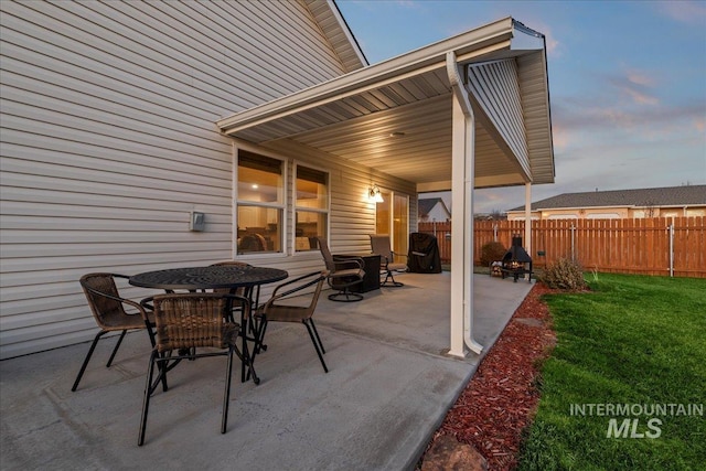 patio terrace at dusk featuring a yard and fence